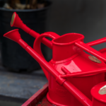 Close-up of several red watering cans in a garden shed, perfect for gardening tasks. - Photo by David Brown on Pexels