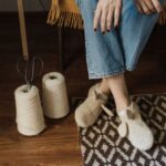 Close-up of woman sitting with handmade slippers, yarn, and scissors on a wooden floor. - Photo by Arina Krasnikova on Pexels