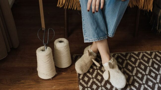Close-up of woman sitting with handmade slippers, yarn, and scissors on a wooden floor. - Photo by Arina Krasnikova on Pexels